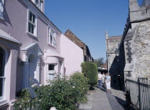 People walking through a narrow path between a pink cottage and a church.European Great Britain Northern Europe UK United Kingdom British Isles Destination Destinations Holidaymakers Religion Religio...