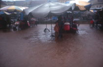 People sheltering under large umbrellas during monsoon floods  water covering the ground.