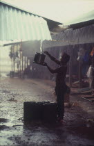 Man collecting rainwater as it runs off a roof above him.