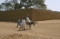 Street scene with two men walking beside a man on a donkey