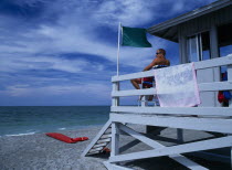 Lido Beach. Lifeguard man sitting on high stall looking out to sea in Lifeguard Hut with Green Flag