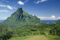 Landscape with dense vegetation and central jagged peak with sea beyond.