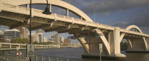 Walkers strolling along the River Walk beneath a road bridge over the Brisbane River.