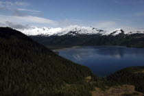 View over tree covered slopes and waters toward snow capped mountain peaks on the other side