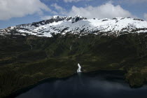 Aerial view over water and tree covered slopes leading toward snow capped mountain peaks