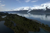 View over trees and calm waters of the bay toward snow capped mountain range