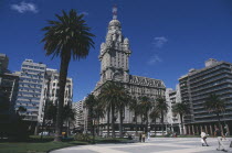 City scene with tree lined square in foreground and mix of old and new buildings behind.