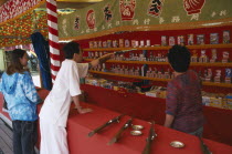 Narita.  Young couple at shooting range pointing out prizes available to win.