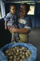 Marquesas Islands.  Taipivai Hiva.  Fermenting noni fruit with woman holding child behind.