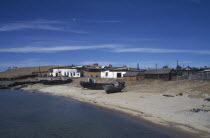 Fishing boats pulled up on lake shore with scattered buildings behind.