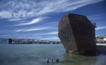 Rusting hull of ship in shallow water at lake shore.