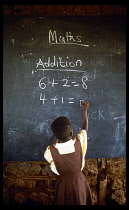 Child in primary school maths class writing sums on blackboard with chalk. addition