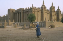 Exterior of mud mosque with man crossing barren ground in the foreground.