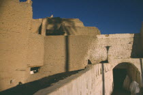 Veiled women walking through passage below mud brick town wallsGadames