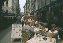 People at outside tables of restaurant with woman reading Hungarian newspaper in the foreground.