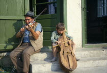 Man and child playing violin and a gardon  a cello like instrument played by hitting the strings with a small stick.