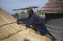 Dinka man thatching hut in cattle camp.