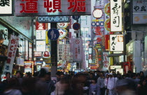 Dotonbori sign illuminated at dusk among mass of other neon signs with crowds of shoppers below