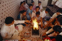 Hindu family participating in head shaving ceremony of young son in domestic interior.