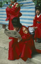 Confucian devotee reading a newspaper during break from rites.