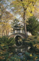 Parc Monceau created by landscape designer Louis Carmontelle.  Arched bridge over stream surrounded by trees.Park