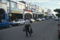 Man crossing King Street towards parked cars and shops