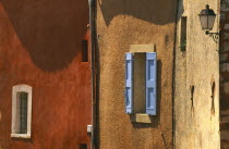 Roussillon.  Architectural detail of ochre and terracotta coloured walls with blue window shutter and wall lamp.