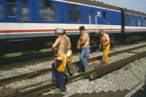 Railway workers standing on tracks as train passes.