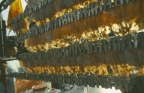 Lines of dryed fish hanging on market stall with seller next to Chao Phrya River.