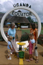 Uganda, Equator, European family watching water go down plughole beside sign.