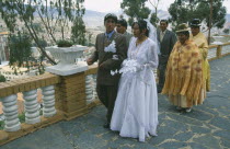 Wedding in El Monticulo. Bride and Groom walking with guests behind.