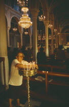 Ermoupolis. The interior of the Catholic Church of Ag. Yiorgios. Candles being lit and people stood at the pews