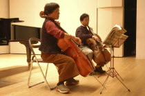 53 year old public health nurse named Teruko Ui plays cello with teacher Satoshi Miyano  at recital as a hobby and for relaxation