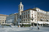 Town square with church and clock tower and cafes with outside tables.