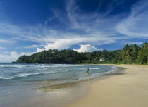 Quiet sandy beach fringed with palm trees on the south coast with fisherman standing in shallow water at shoreline and building amongst trees behind.