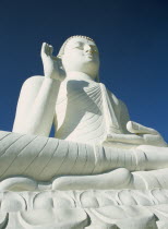 Angled view of large white seated Buddha seen from below looking up.