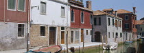 Murano Island.  View along canalside houses with boats moored to posts in front.