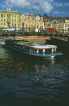 Moika Canal with tour boat passing underneath arched bridge with cars crossing and traditional houses behind.