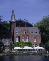 View across Minnewater or Love Lake  towards red brick building with tiled  turreted roof with gabled windows.