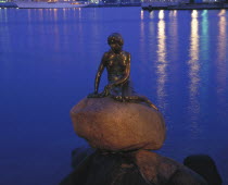 The Little Mermaid statue at night with lights reflected in the water