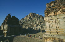 Achyutaraya Temple with Matanga Hill in the background and people walking between buildings in the foreground.