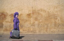 Woman with veil waliking past colourful wall.