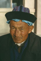 Head and shoulders portrait of a Tibetan man wearing a hat