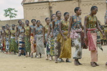 Line of female dancers wearing colourful textiles at festival and watching crowd behind.Colorful Zaire