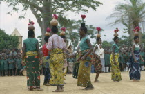 Dancers at festival carrying gourds and bottles filled with flowers on their heads and watching crowd behind. Zaire