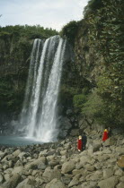 Couples in traditional dress at rocky foot of waterfall.