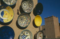 Painted ceramic dishes displayed on wall with Kasbah Taorirt partly seen behind.