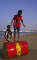 Two young Omani boys playing on an abandoned Shell oil drum on the beach.