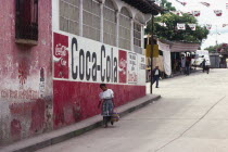 Indigenous woman walks down street past a Coca Cola street sign.