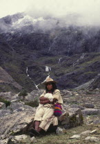 Ica Indian with lamb sat on a rock  surrounded by mountains.